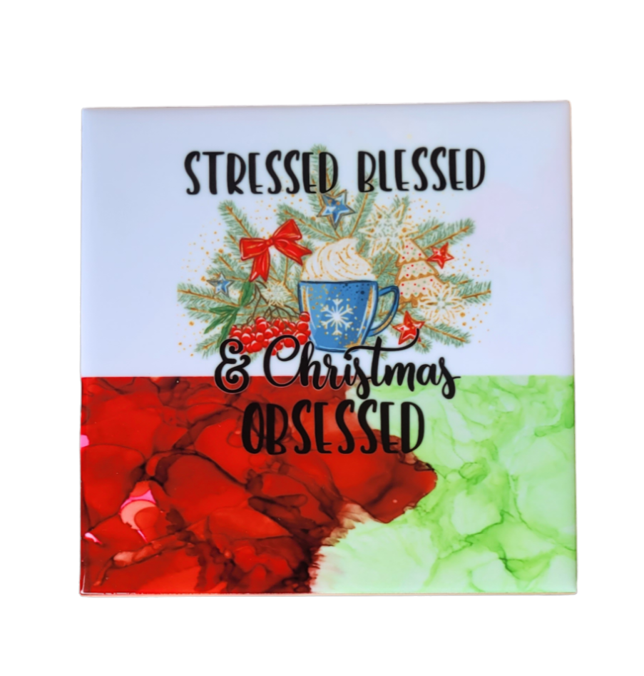 4.5 x 4.5-inch ceramic tile Christmas Coaster with a white background at the top and green alcohol ink background at the bottom. It has a coffee mug and   greenery and bows with the words "Stressed Blessed & Christmas Obsessed