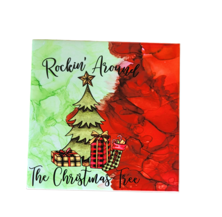 4.5 x 4.5-inch ceramic tile Christmas Coaster with red and green alcohol ink background. It has a Christmas tree and gifts with the words "Rockin Around The Christmas Tree