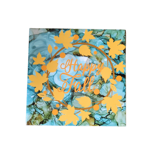 8x8-inch ceramic tile display with a blueish-green color alcohol ink background with golden color leaves on a circle shaped vine and  the words Happy Fall