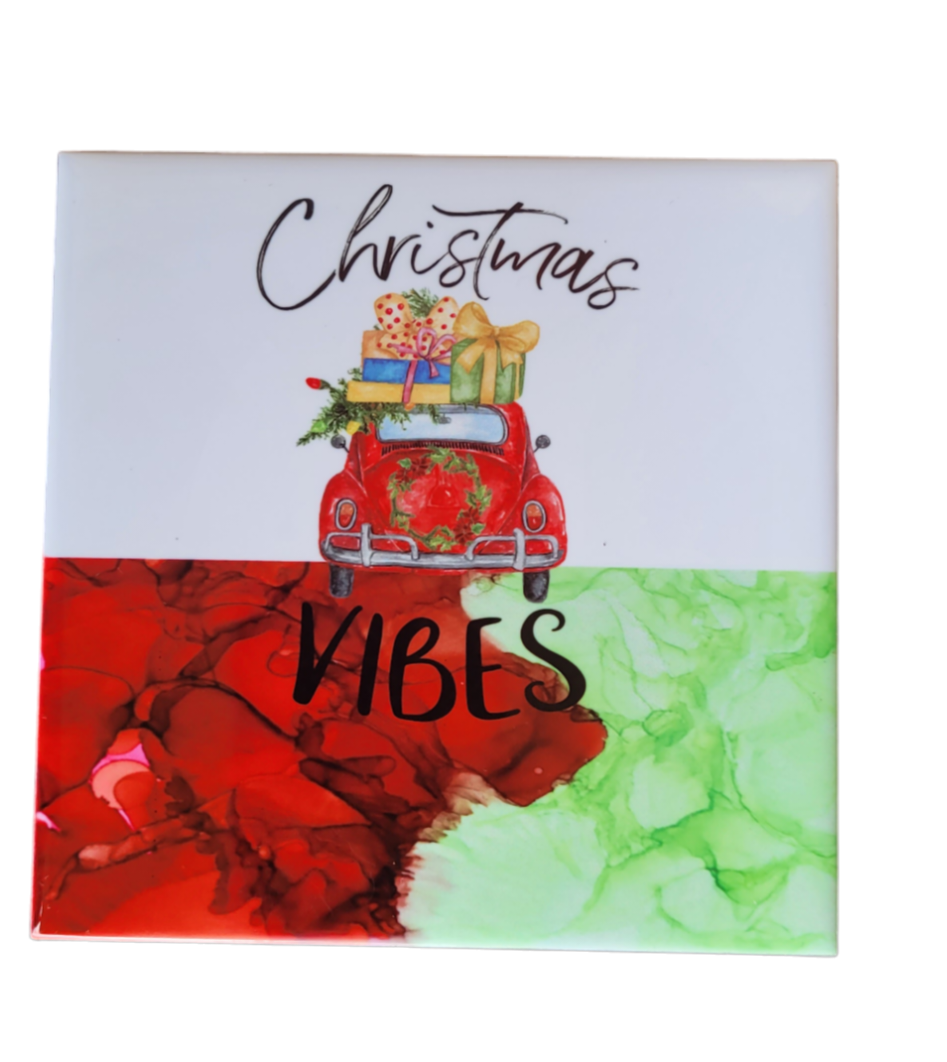 4.5 x 4.5-inch ceramic tile Christmas Coaster with a white background at the top and a red and green alcohol ink background at the bottom. It has the back of a red car with gits on the hood and a wreath around the spare tire with the words "Christmas Vibes."