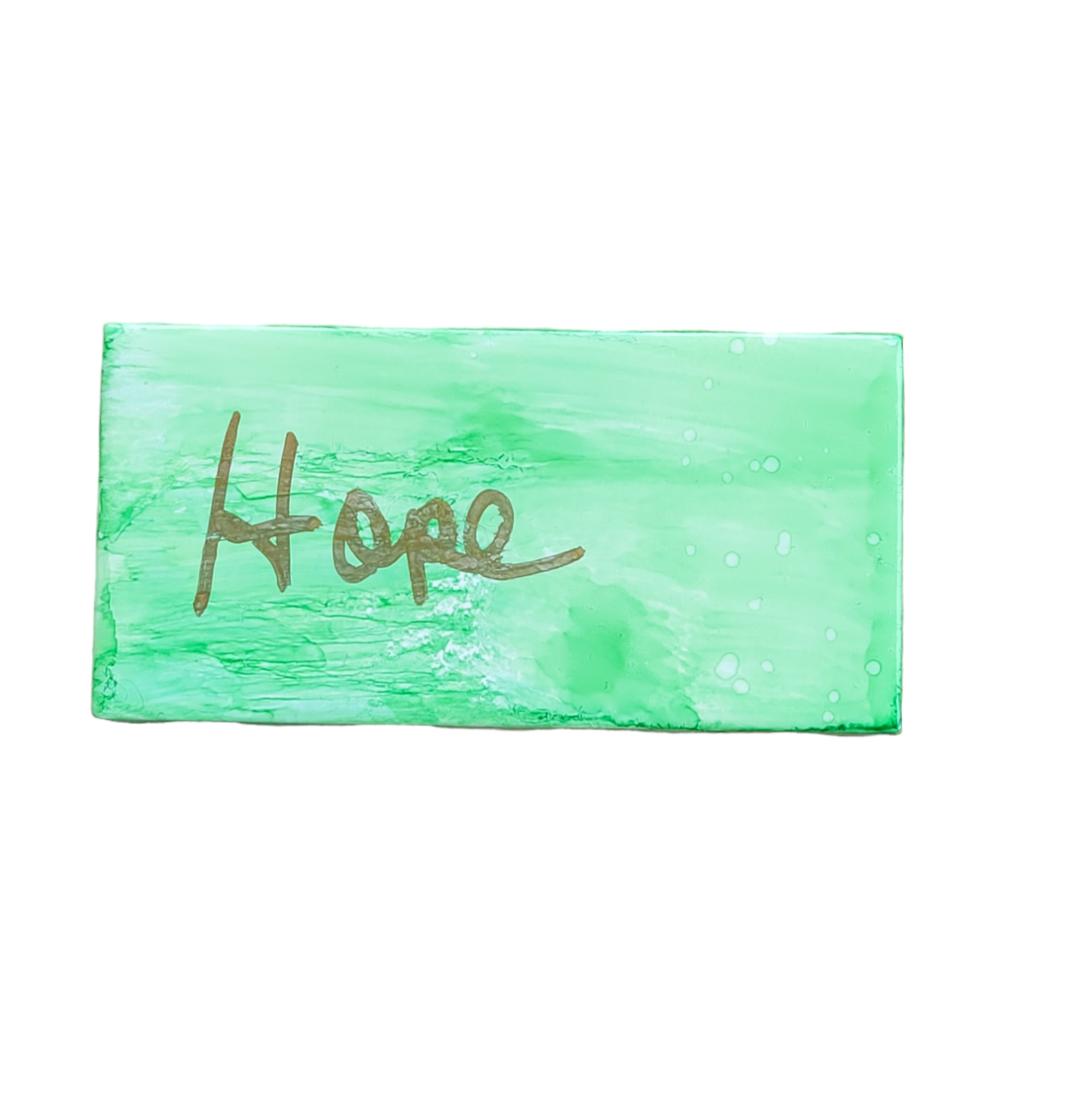 A 3X 6-inch ceramic tile with the word Hope handwritten on a distressed looking background that has been painted with green alcohol ink.